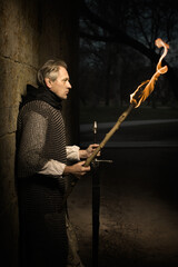 Medieval infantry armed man on guard in castle gateway with lit torch