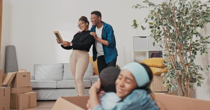 The siblings are sitting in a large paper box left over from the move, the children are playing, cuddling, laughing, in the background the parents are looking at the souvenirs they found