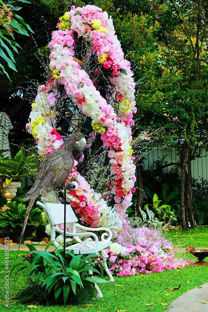 Wall mural Magnificent pink roses ornamented nearby a white long bench with a metal parrot standing on a pole along path walk in a romantic  garden