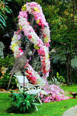 Magnificent pink roses ornamented nearby a white long bench with a metal parrot standing on a pole along path walk in a romantic  garden