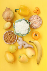 Yellow fruits and vegetables on a yellow background. Pears, raisins, lemon, bergamot, apples, ginger root, paprika, cauliflower, kumquat, peeled dried peas, tomato, banana. Top down view. Closeup
