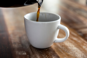 Pouring coffee into white mug on a wood table.