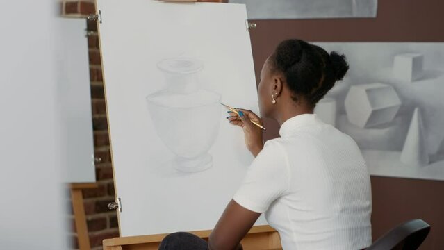 African american woman drawing professional sketch on canvas, using pencil and artistic equipment in art class program. Learning to draw sketch to develop skills for growth. Handheld shot