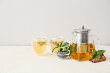 Teapot and glasses of tasty tea on light background
