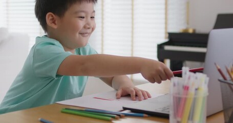 Cute pupil child gen z alpha boy sit talk video call self e-learning lesson on laptop at home table. Asia art school tutor class drawing color pencil in paper watch fun social media upskill kid.     