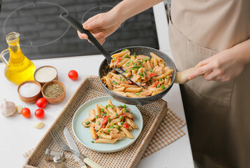 Woman putting cajun chicken pasta in plate in kitchen