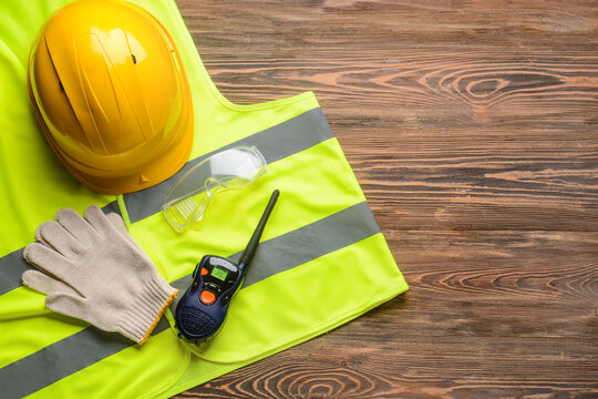 Safety equipment with protective vest and radio transmitter on wooden background