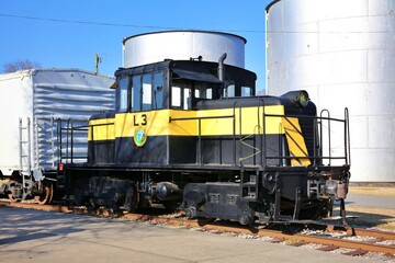 Vintage 1940s era locomotive used in the rail yard to move equipment, sitting on a track hooked to a car.  