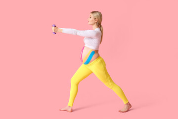 Pregnant woman with applied kinesio tape training against color background