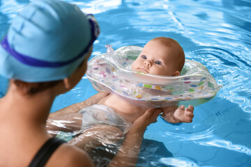 Young woman and her adorable baby with inflatable ring in swimming pool
