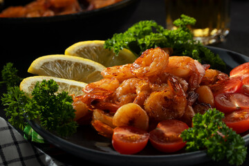 Fried shrimps with lemon, tomatoes and herbs on a plate on the table, close up
