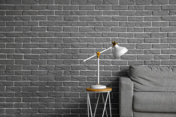 Modern lamp on coffee table and sofa near grey brick wall