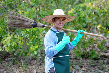 Asian man gardener is at garden, holding broom on shoulder. Thumb up. Concept : Eco friendly...