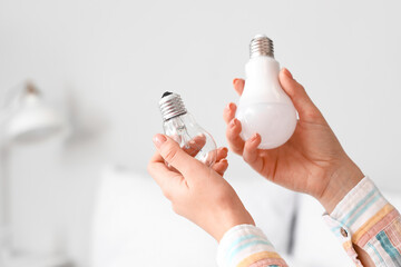 Woman holding different light bulbs in bedroom, closeup