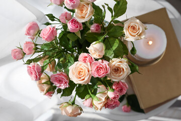 Vase with bouquet of roses and burning candle in room