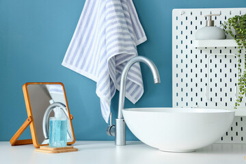 Table with sink, mirror, soap and pegboard near blue wall