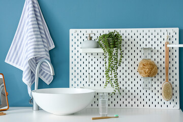 Table with sink, glass of water, toothbrush and pegboard near blue wall