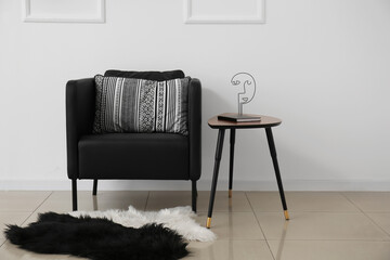Black armchair, table with book and decor near light wall