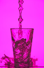 Pouring of clear water in glass on color background
