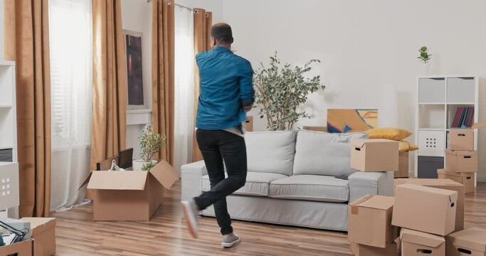 Happy handsome man full of joy jump dances in the new apartment moves, cardboard boxes scattered in the living room, practicing choreography, rhythmic movements, spinning on its axis