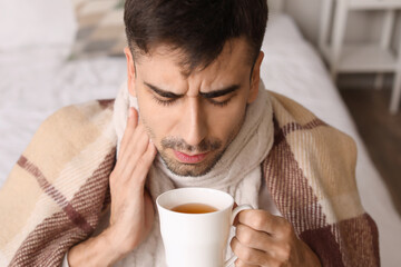 Ill young man with sore throat drinking hot tea at home