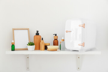 Shelf with small refrigerator and cosmetic products hanging on color wall