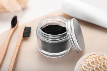 Jar with activated charcoal tooth powder and toothbrushes on table, closeup