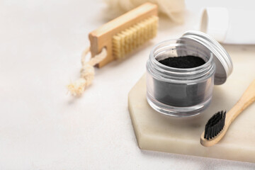 Jar with activated charcoal tooth powder and toothbrush on light background, closeup
