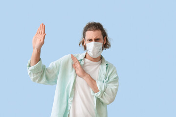 Young man in medical mask avoiding something on color background