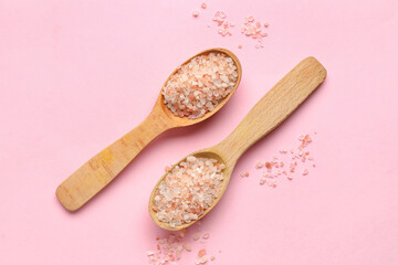 Wooden spoons with sea salt on pink background