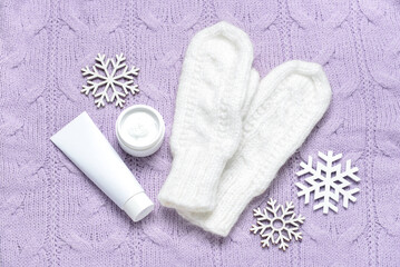 Fototapeta na wymiar Mittens, cosmetic products and snowflakes on knitted fabric background