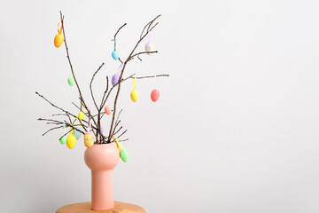 Vase with tree branches and Easter eggs on light background