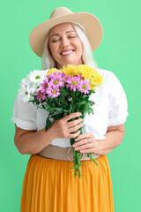 Happy mature woman holding bouquet of beautiful flowers on green background. International Women's Day celebration