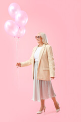 Mature woman holding air balloons on pink background. International Women's Day celebration