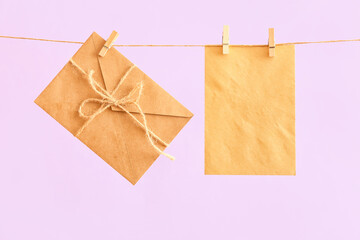 Blank card and envelope hanging on rope against color background. International Women's Day celebration