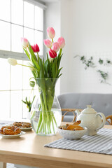 Vase with beautiful tulip flowers on dining table in room