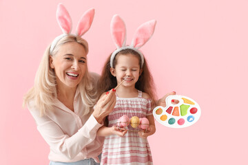 Obraz na płótnie Canvas Happy little girl and her grandmother with Easter eggs and paints having fun on color background