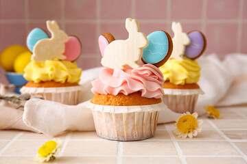 Tasty Easter cupcakes and flowers on color background, closeup