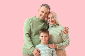 Little boy with his grandparents in warm sweaters hugging on pink background