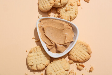 Tasty peanut cookies and bowl with butter on beige background