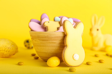 Bowl with tasty Easter cookies in shape on bunny candies on yellow background