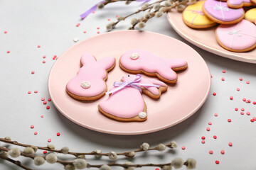 Plate with tasty Easter cookies in shape on bunny and pussy willow branches on light background