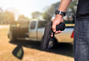 Semi-automatic black 9mm pistol gun holding in hands of gun shooter with blurred pickup car in the...