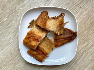 Deep fried fish in the white plate on the floor. Delicious homemade meal. Close up. Blurred.