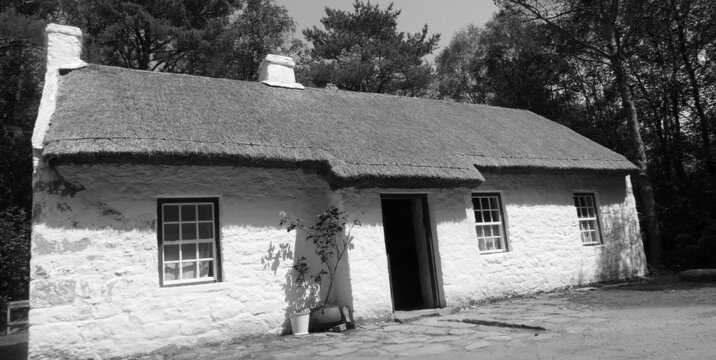 Black and white photo of an Old Irish Traditional Whitewashed Cottage with thatched roof on a Farm in Ireland