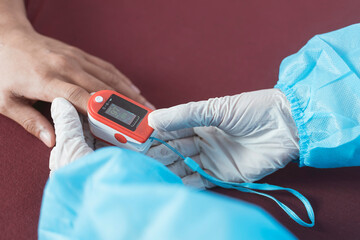 A nurse in PPE gear inserts an Oximeter on a patient's index finger. Checking blood oxygen or SpO2 levels. At the emergency ward of a hospital.