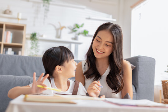 Happy Asian little girl doing homework with mother at home. Asian young mother teaching small daughter to drawing reading and writing to develop her daughter skill. Home School Concept