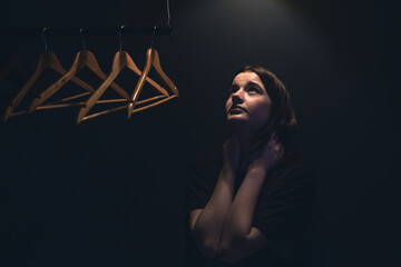 A young woman near empty hangers in the dark under a lamp.