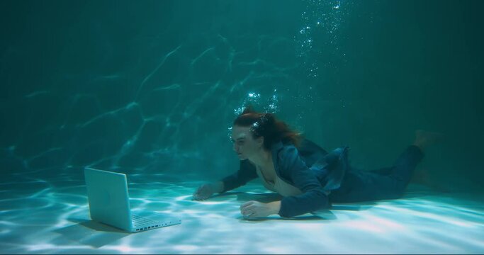 Young happy determined beautiful workaholic boss business woman in suit dives underwater to work with laptop slow motion