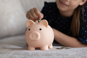 Obraz na płótnie Canvas Child dropping coin into toy pink piggybank. Smart girl saving money, collecting cash for future purchase, learning economy, business, investment, counting budget. Financial planning concept. Close up